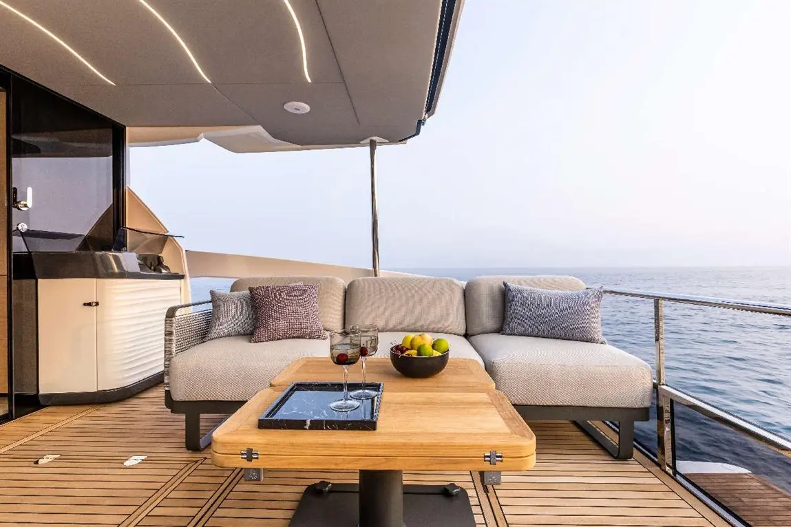 Luxury yacht terrace with a plush sofa, drinks, fruits, and a stylish wooden table, overlooking a serene sea view.